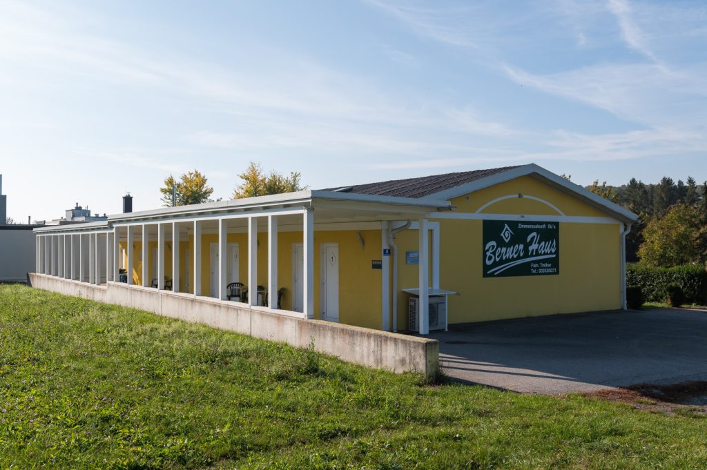 Gelbes Gebäude mit Säulengang und Schild "Berner Haus" in grüner Umgebung.