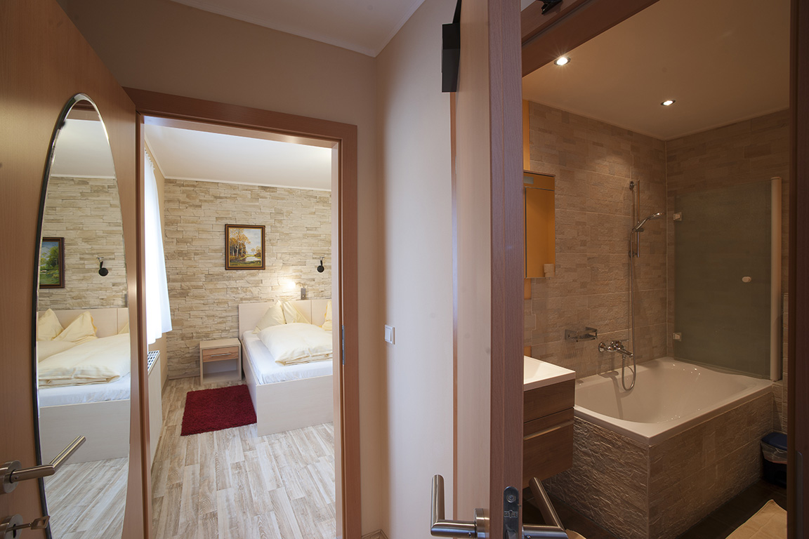 Offene Suite mit Blick vom Eingang auf das Doppelbett und das angrenzende Badezimmer im Gasthaus Treiber.
