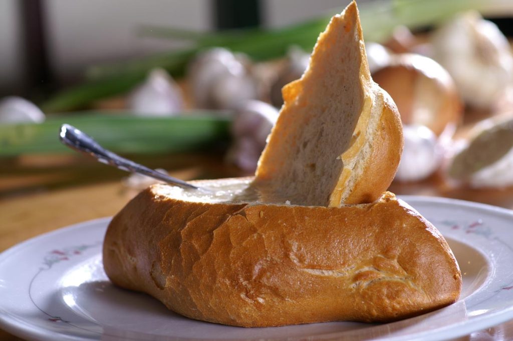 Eine Knoblauchsuppe im Brotlaib mit einem Löffel, arrangiert auf einem rustikalen Holztisch.