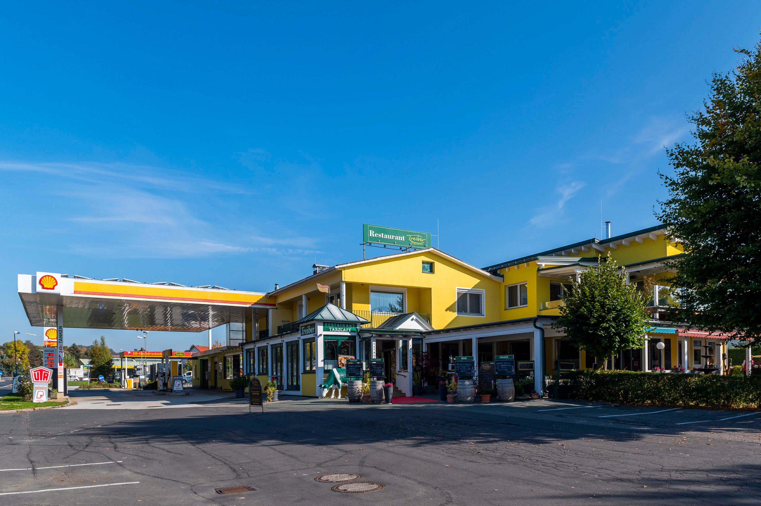 Gelbes Gasthaus mit Restaurant und angegliederter Shell-Tankstelle unter blauem Himmel.