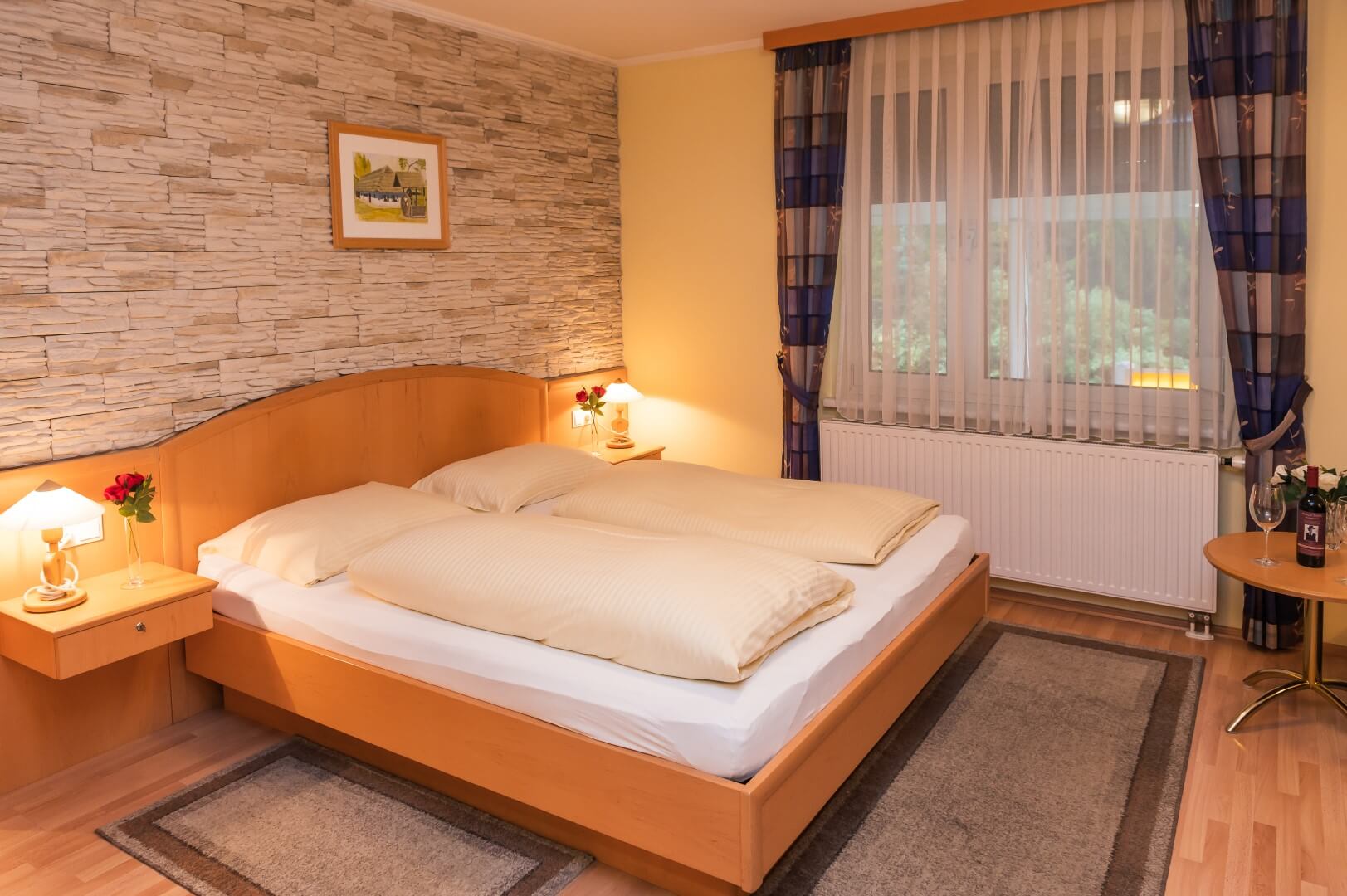 Gemütlich eingerichtetes Zimmer mit Doppelbett, Steinwand, Nachttischen und Fensterblick ins Grüne im Gasthaus Treiber.