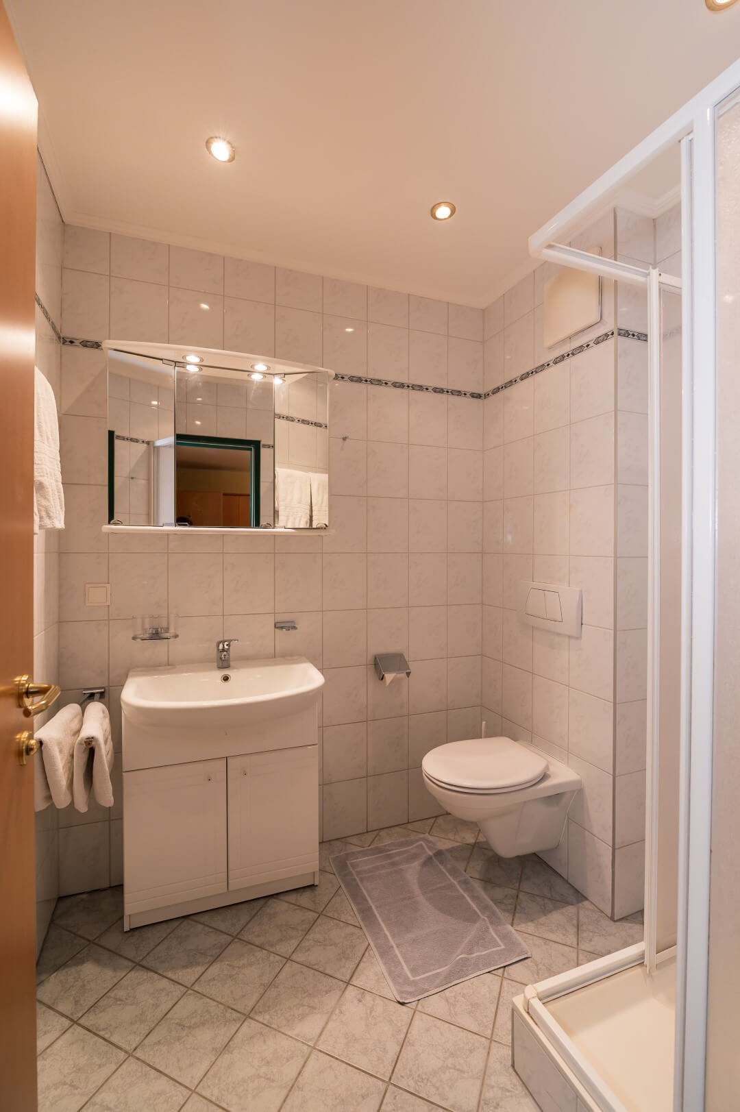 Helles Badezimmer mit Duschkabine, Waschtisch und Spiegel im Gasthaus Treiber.