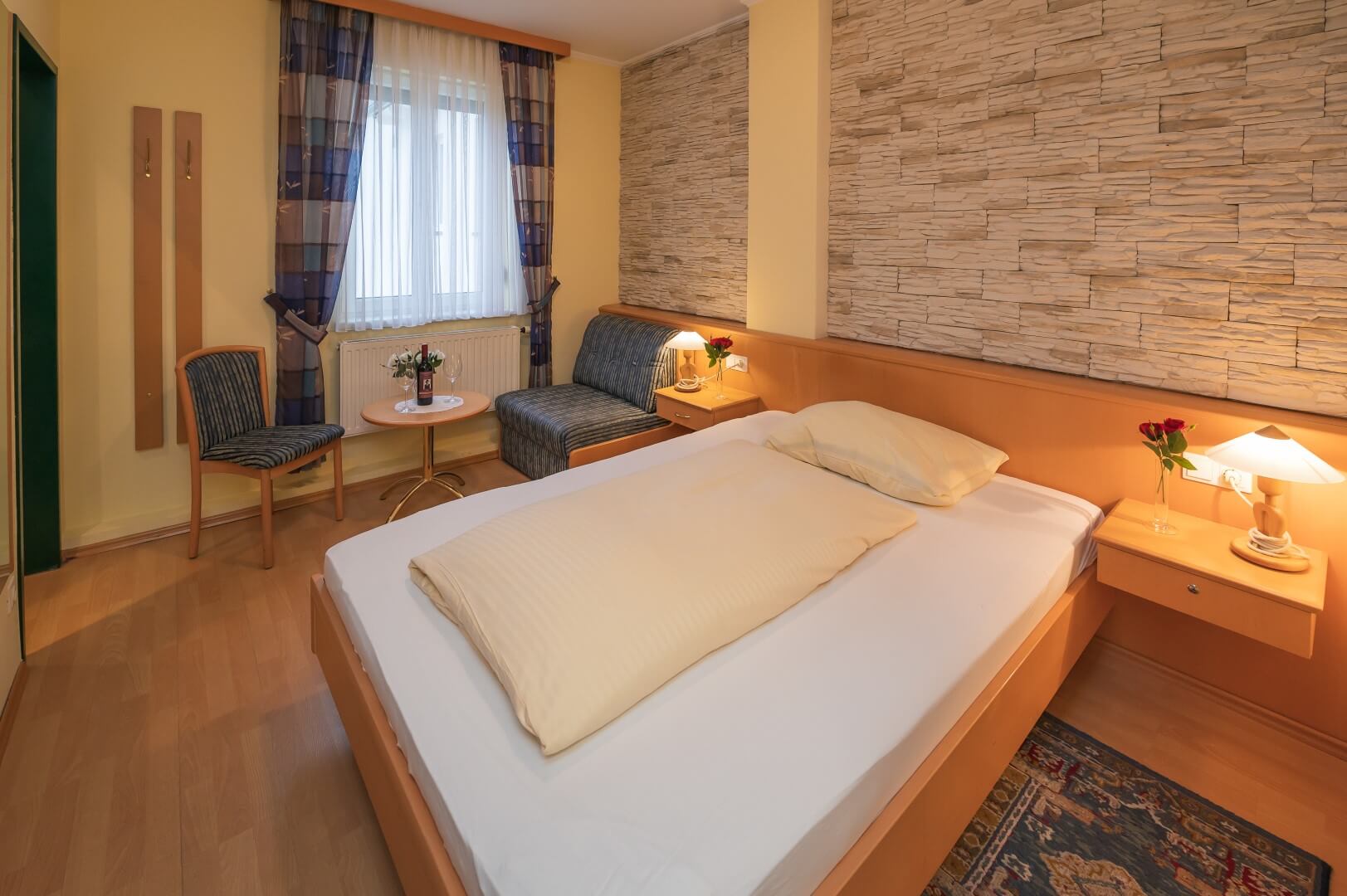 Einladendes Zimmer mit Doppelbett, gemütlicher Sitzecke und Steinwand im Gasthaus Treiber.