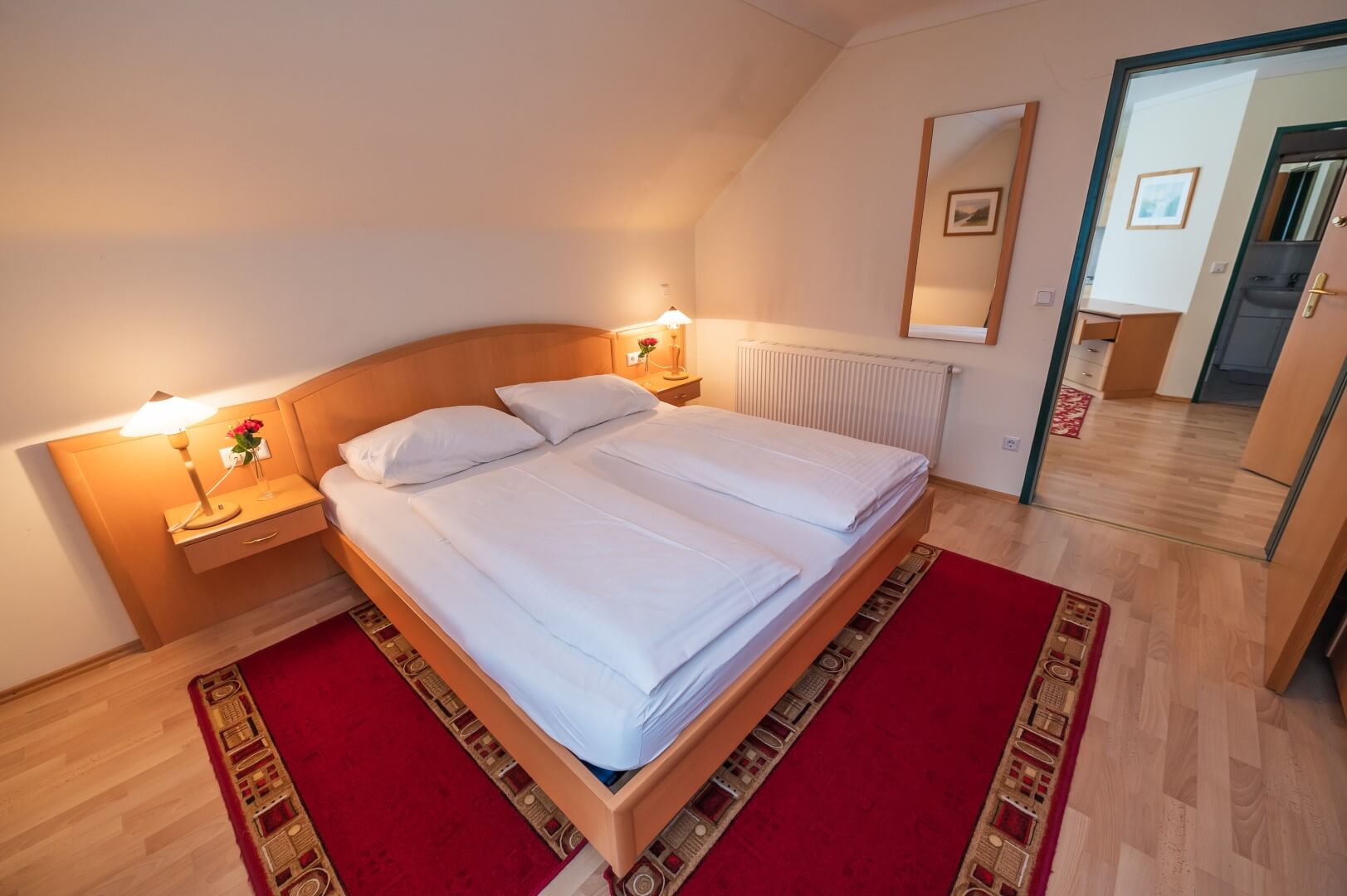 Ein gemütliches Doppelzimmer mit Parkettboden, warmen Farben und angrenzendem Badezimmer im Gasthaus Treiber.