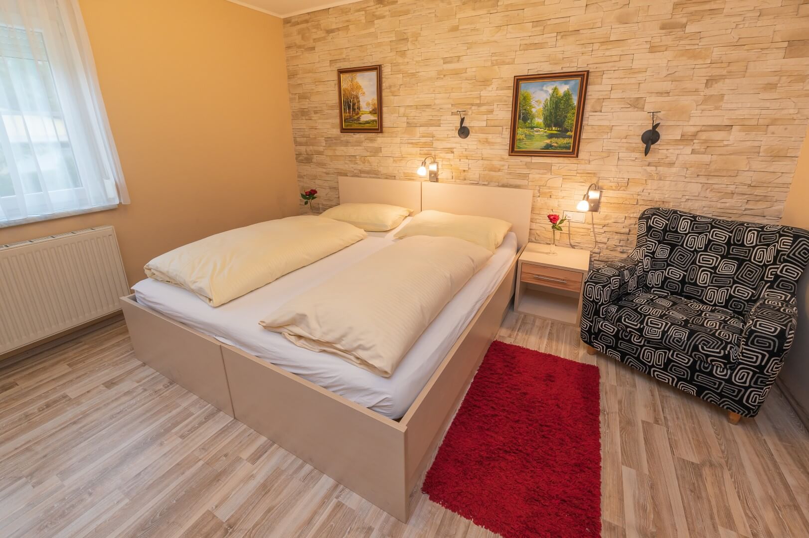 Warm beleuchtetes Zimmer mit großem Bett, Steinwand und einer gemusterten Sitzgelegenheit im Gasthaus Treiber.