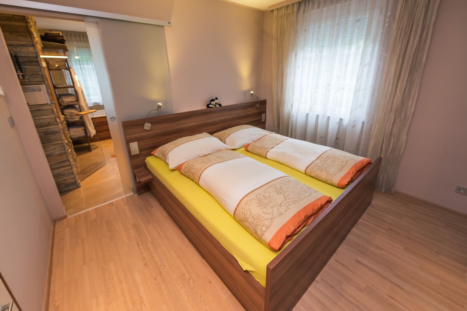 Ein einladendes, helles Zimmer mit Doppelbett, gelber Bettwäsche und Holzelementen im "Haus Michaela".