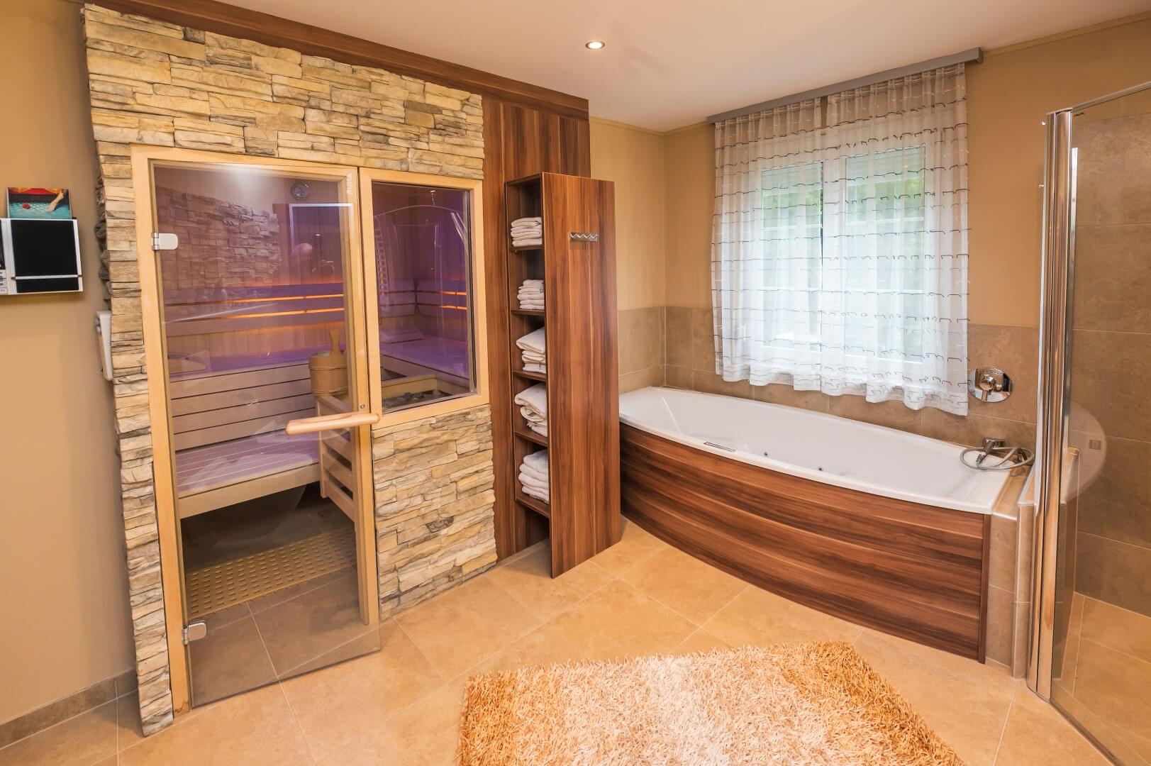Ein moderner Wellnessbereich mit Sauna und Eckbadewanne, umgeben von warmen Holz- und Steinakzenten.