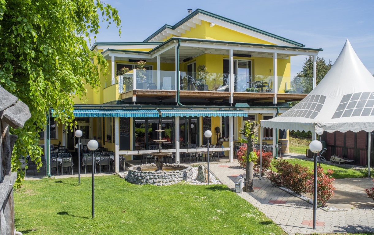 Tageslichtansicht des Gasthaus Treiber mit seiner gelben Fassade, umgeben von grünen Bäumen und einer einladenden Außenterrasse.