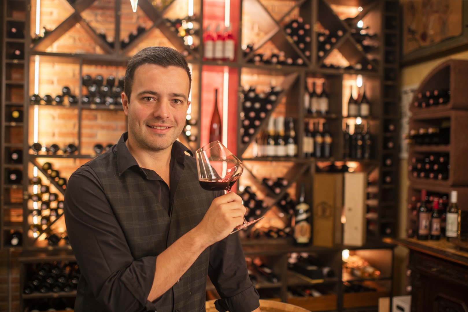 Herbert Treiber Jun. lächelt, während er in einem traditionellen Weinkeller ein Glas Rotwein hält.