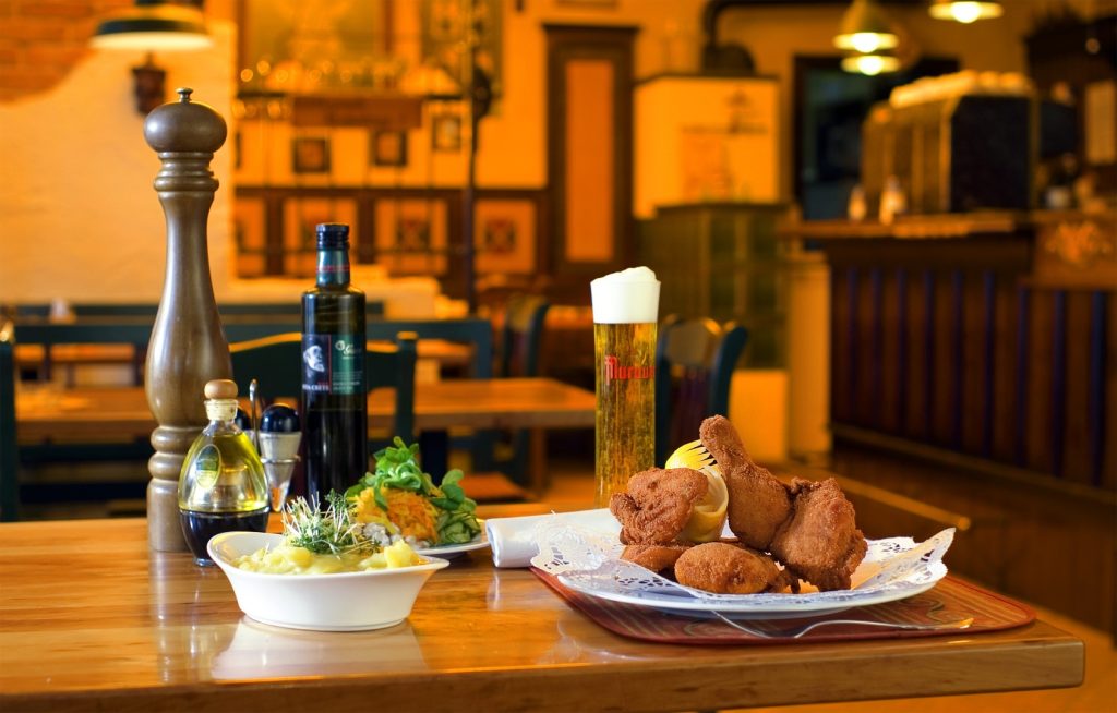 Traditionelles österreichisches Backhendl mit Kartoffelsalat, serviert auf einem Holztisch neben einem frisch gezapften Bier und Gewürzen.