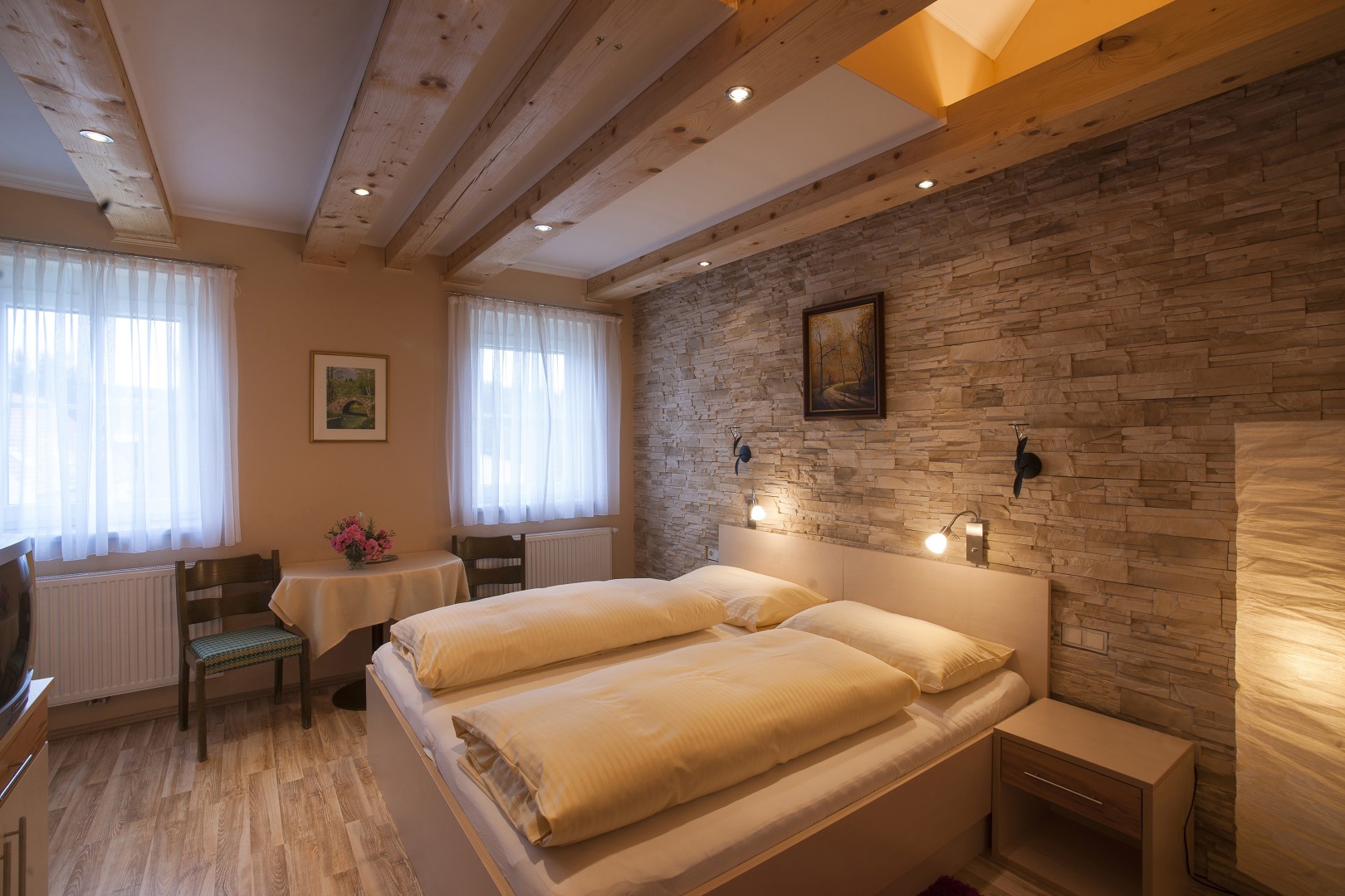Behagliches Zimmer mit Naturholzbalken, gemütlichem Doppelbett und Steinwand im Gasthaus Treiber.