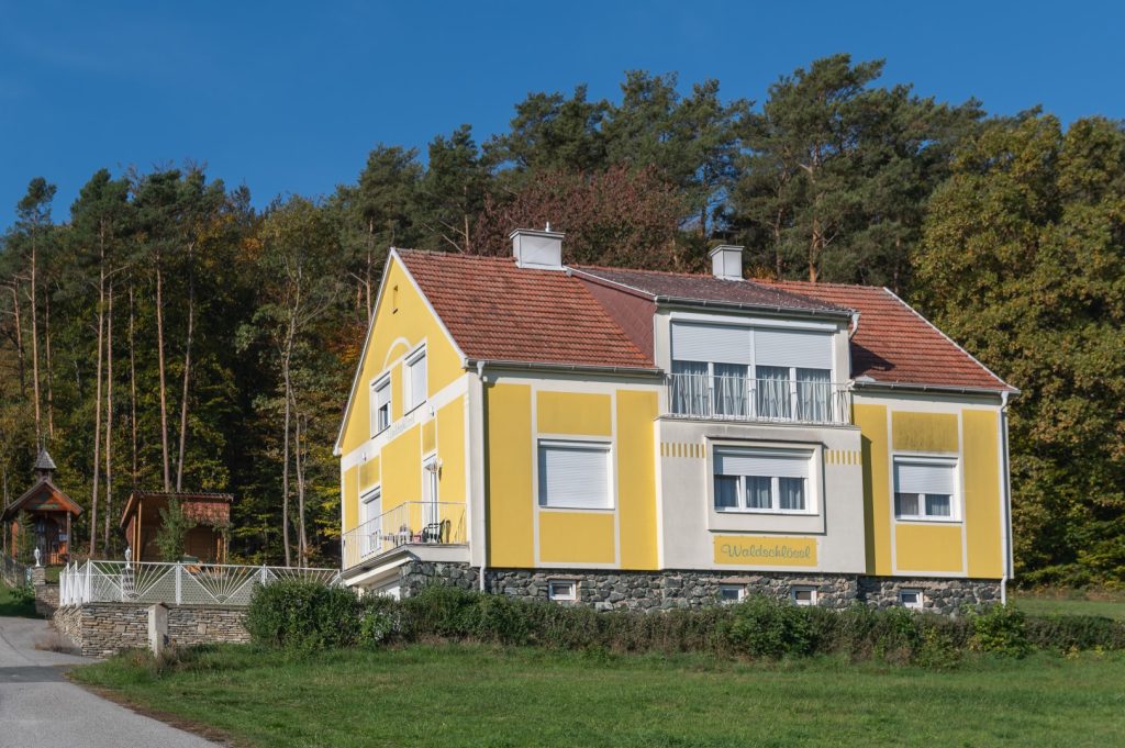 Zwei-stöckiges Gästehaus in Gelb mit Waldrand im Hintergrund.