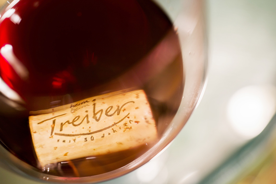 Ein Weinkorken mit der Aufschrift "Gasthaus Treiber" ruht in einem Glas mit rotem Wein.