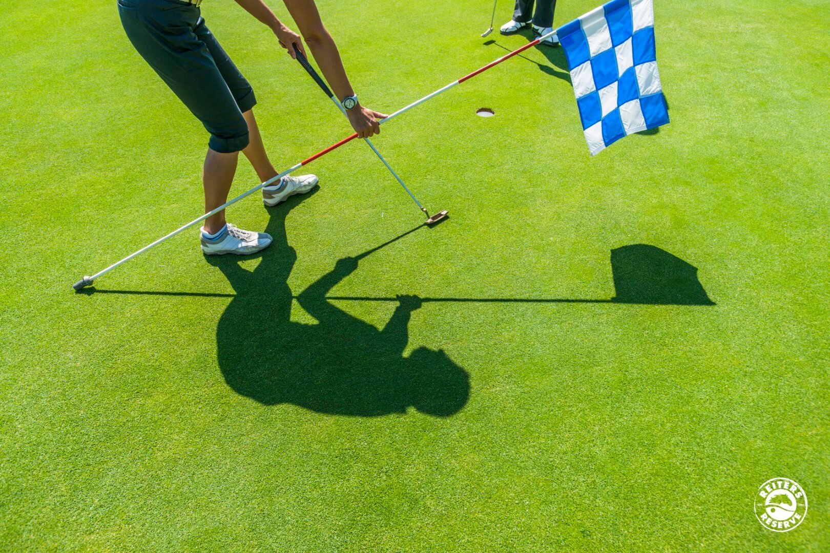 Ein Golfer, der im Begriff ist, auf einem sonnigen Golfplatz einzulochen, mit dem Schattenbild klar im Vordergrund.