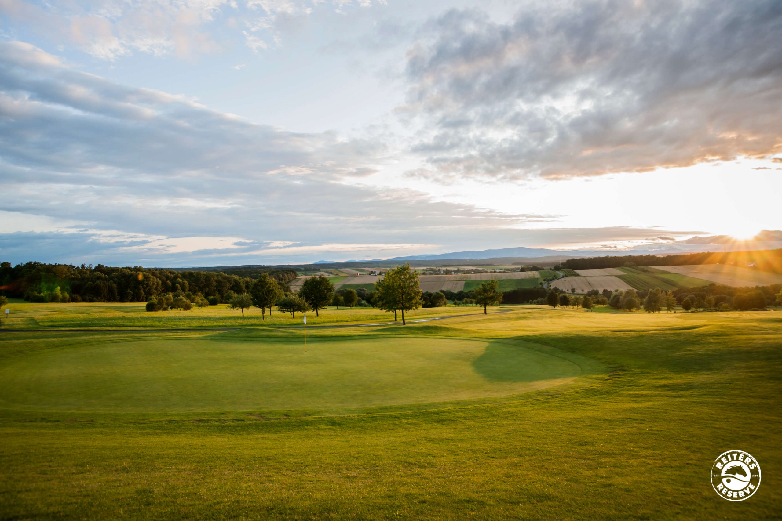 Ein weitläufiger Golfplatz bei Sonnenuntergang, der eine friedliche Atmosphäre ausstrahlt.