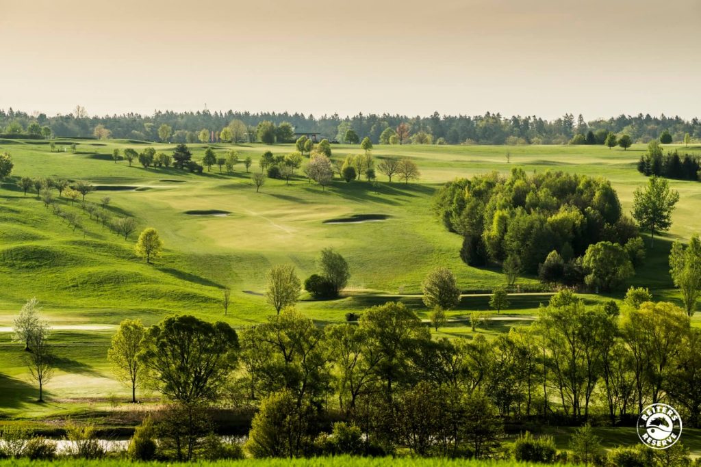 Hügeliger Golfplatz mit üppigen grünen Fairways und Bäumen bei Tageslicht.