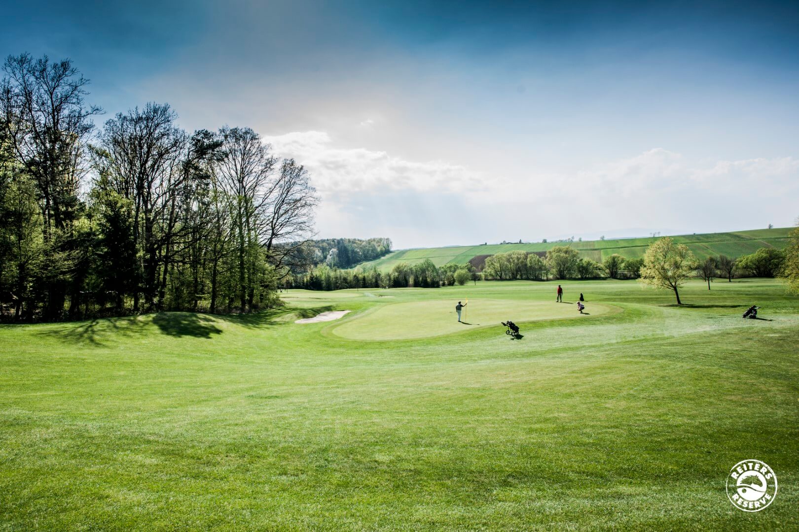 Golfspieler in einer weiten, hügeligen Landschaft, die das Grün eines gepflegten Golfplatzes genießen.