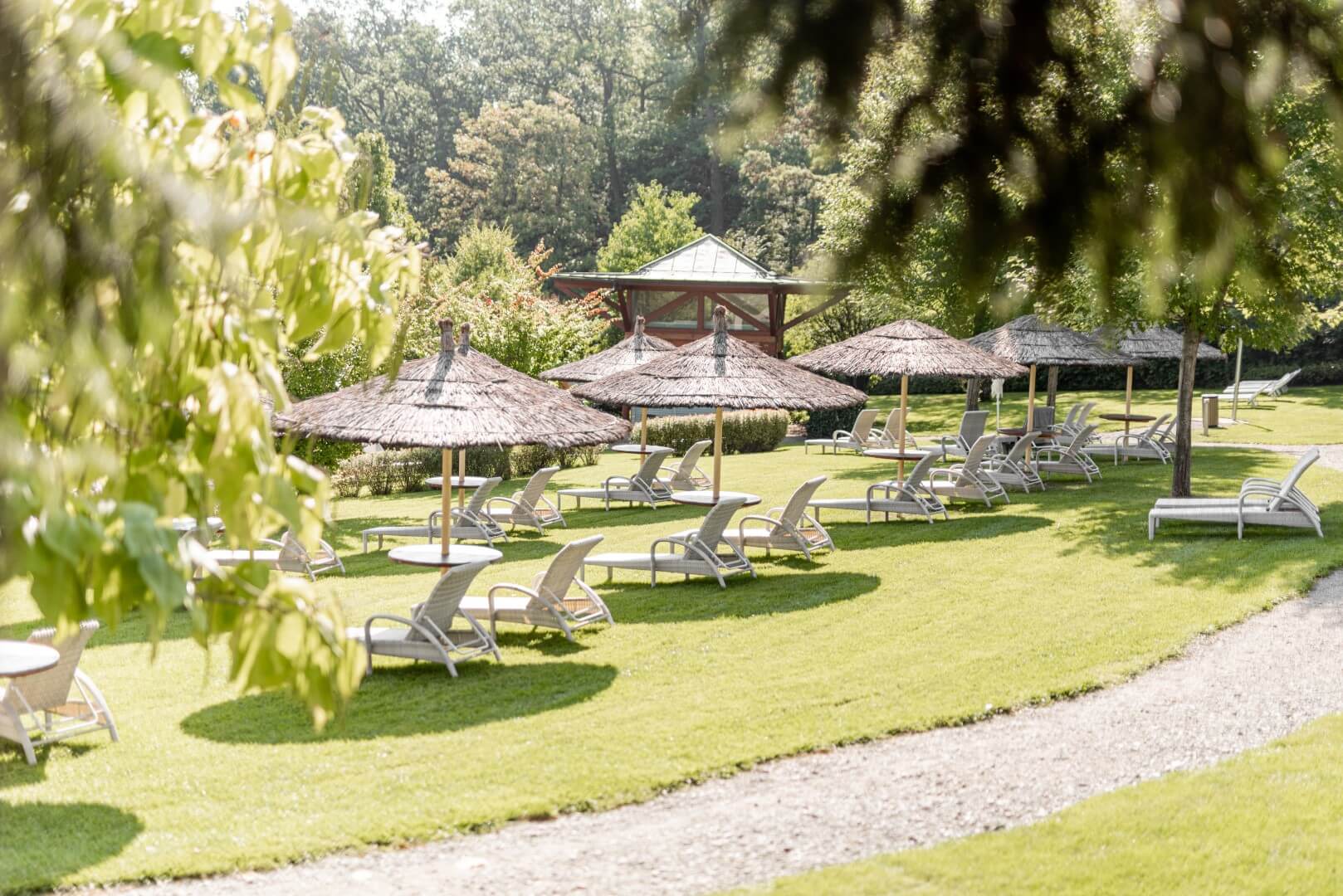 Ein idyllischer Garten mit Strohschirmen und Liegestühlen lädt zum Entspannen unter freiem Himmel ein.