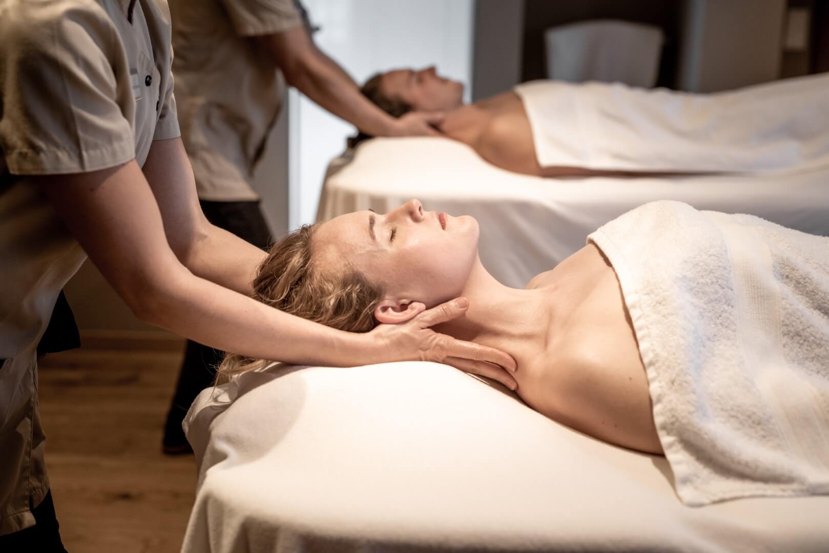 Eine Person erhält eine entspannende Nackenmassage auf einer Liege in einem wohligen Massagezimmer.