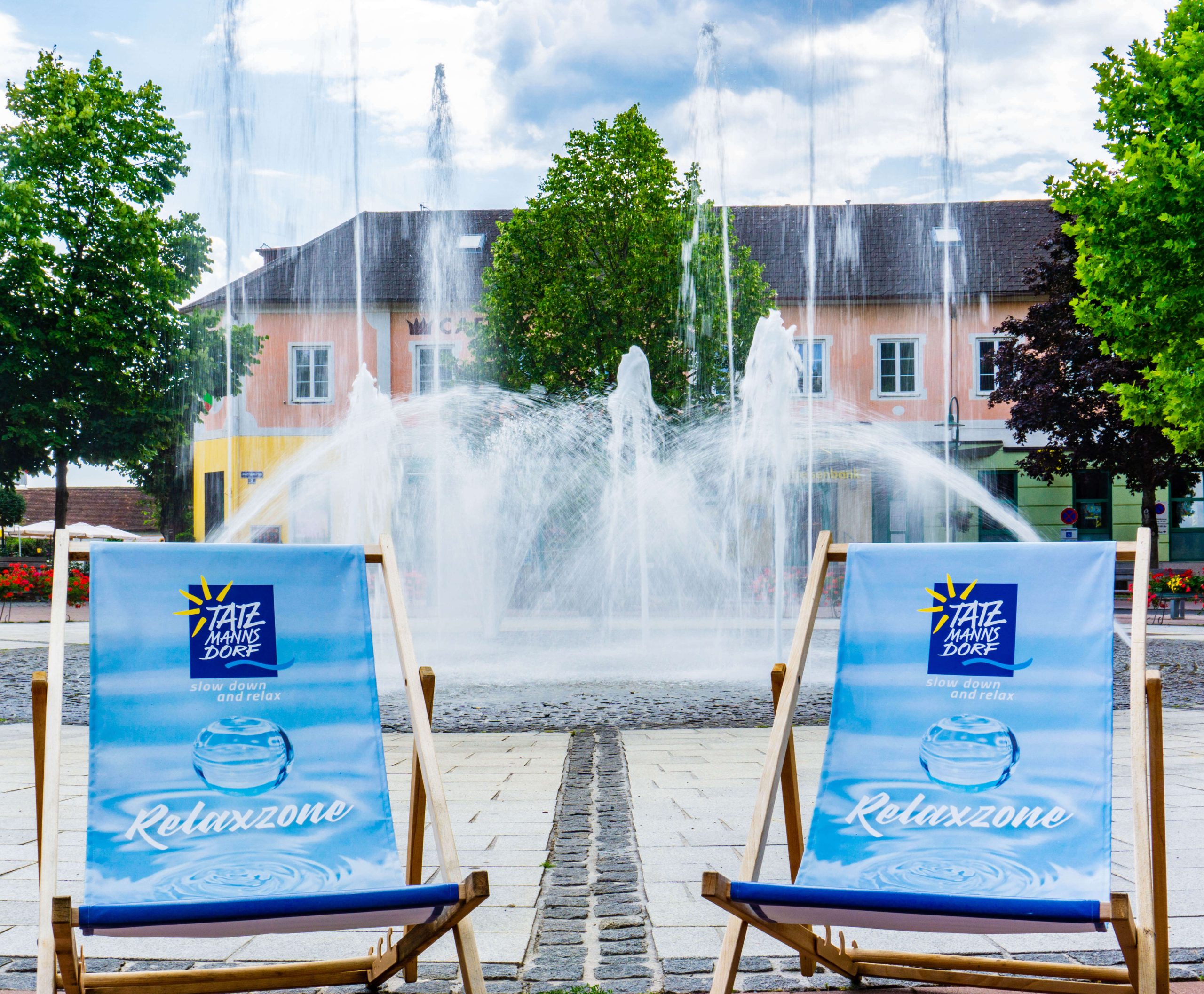 Zwei Liegestühle vor einer sprudelnden Wasserfontäne mit der Aufschrift "Relaxzone" auf den Stühlen.