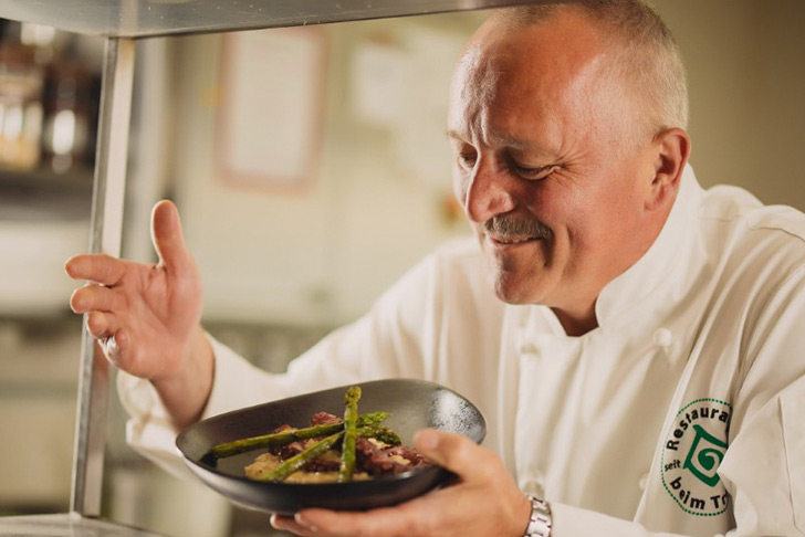 Küchenchef des Gasthaus Treiber präsentiert stolz ein sorgfältig angerichtetes Gericht in der Küche.